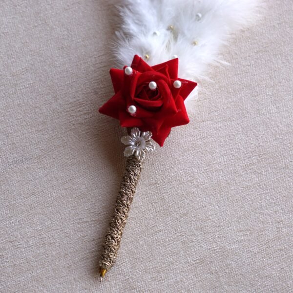 DSC07681 “Close-up of a decorative Nikah signing pen featuring a glittery lace-wrapped barrel, a red artificial rose with pearl-studded floral accents, and white feather plumes.”